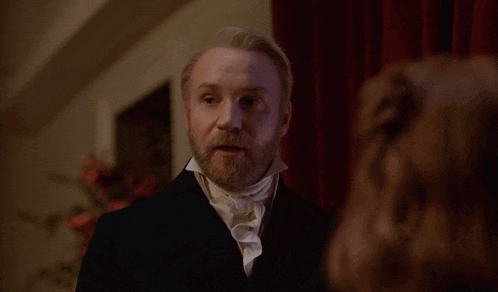 a man with a beard is talking to a woman in a room