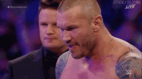 a man without a shirt is standing next to another man in a wrestling match .