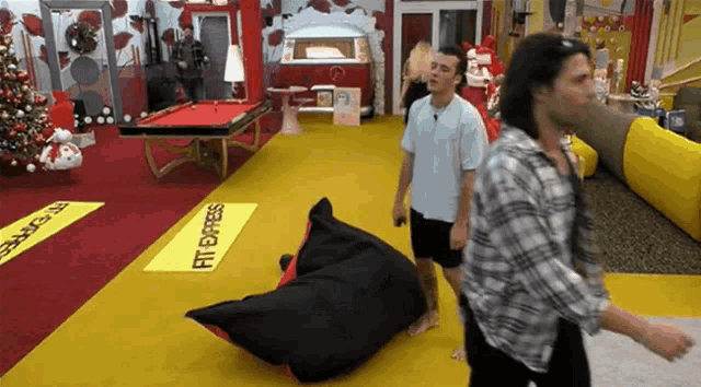 three men are standing in a room with a pool table and a yellow sign that says fit express