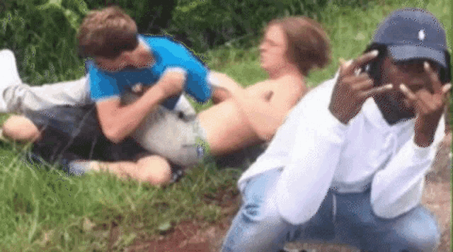 a group of young men are sitting in the grass and one of them is wearing a polo hat .