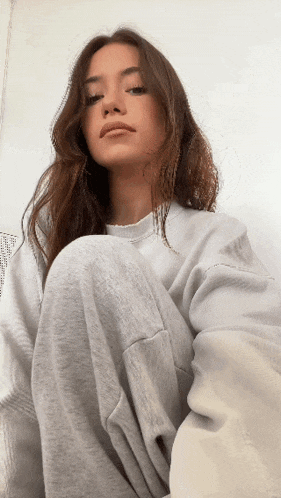 a woman wearing a white sweatshirt and grey sweatpants is kneeling down and looking at the camera