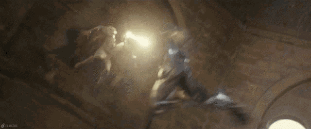 a group of people are fighting in a dark room with a light coming from the ceiling .