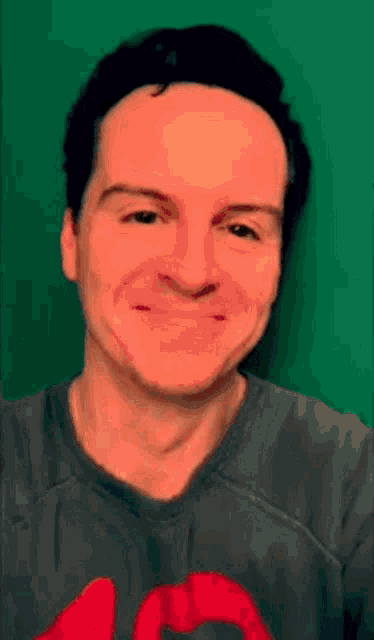 a man wearing a gray shirt with a red heart on it is smiling against a green background .