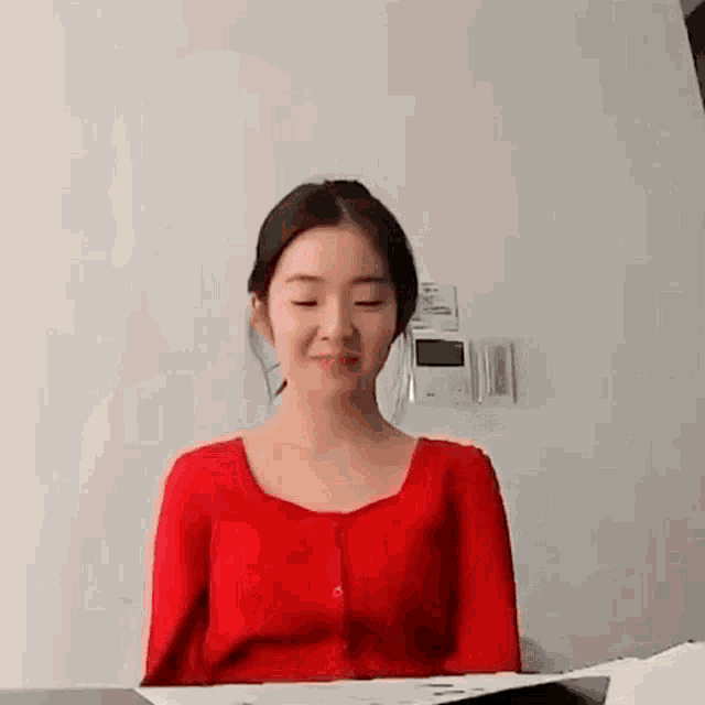 a woman in a red shirt is sitting at a table with her eyes closed and smiling .