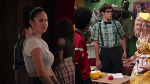 a woman in a crop top and a man in suspenders are standing in a classroom .
