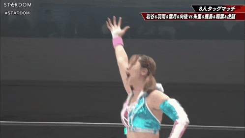 a female wrestler in a blue and pink outfit holds her arms up in the air .