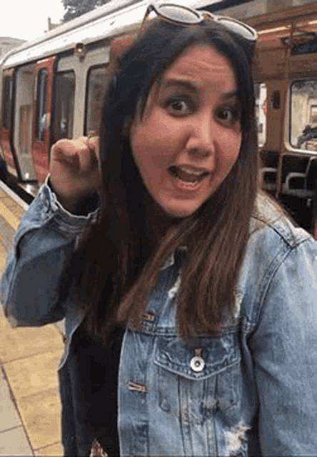 a woman in a denim jacket is standing on a train platform .