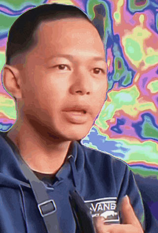 a man wearing a blue vans sweatshirt talks to someone