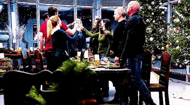 a group of people are sitting at a table with a christmas tree in the background and toasting .