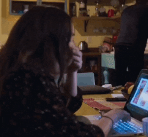 a woman is sitting at a table talking on a cell phone while using a laptop computer .