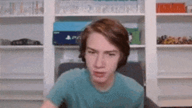 a young man in a blue t-shirt is sitting in front of a playstation box .