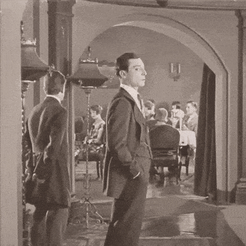 a man in a suit and tie is standing in a hallway talking to another man