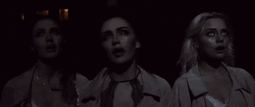 three women are standing next to each other in a dark room and looking up .