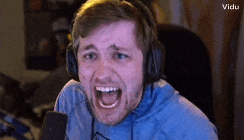 a man wearing headphones and a blue shirt is screaming into a microphone .