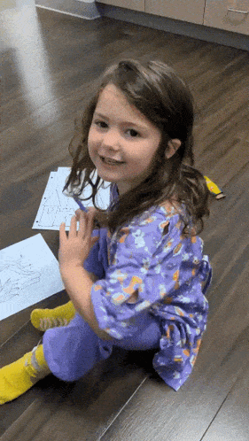 a little girl sitting on the floor with a drawing of a house on the floor