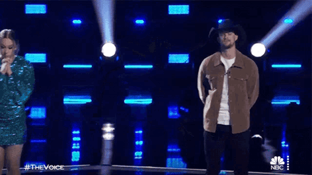 a man wearing a cowboy hat and a brown jacket stands in front of a spotlight .