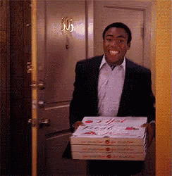 a man in a suit is carrying three pizza boxes in front of a door with the number 305 on it