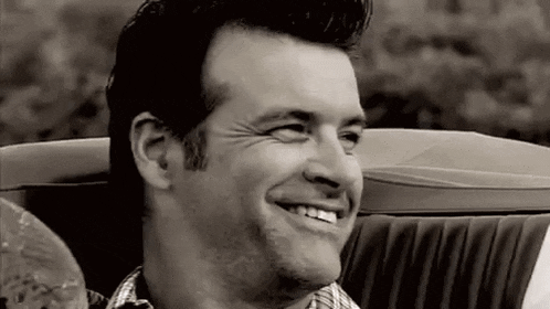 a man is smiling in a black and white photo while sitting in a convertible car .