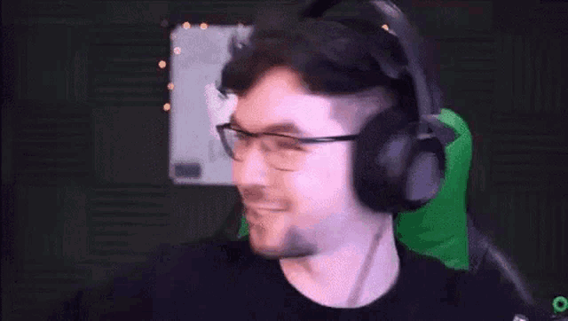 a man wearing headphones and glasses is smiling in front of a white board .