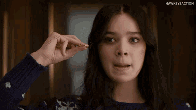 a woman in a blue sweater is making a funny face with her hand in the air .