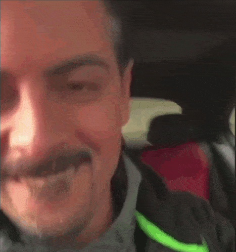 a man with a mustache is making a funny face in a car