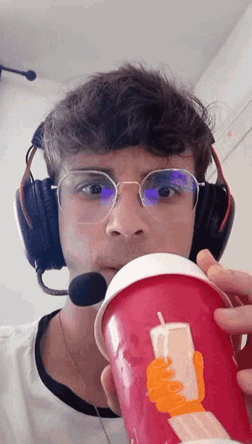 a man wearing headphones and glasses is drinking from a cup with a hand on it