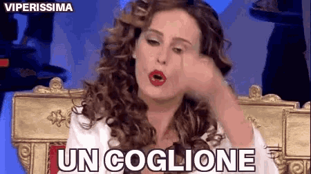 a woman with curly hair is sitting on a throne with the words un coglione written on her face .