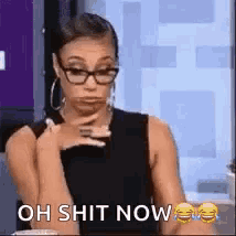 a woman wearing glasses and a black tank top is holding her hand to her chin and says oh shit now .