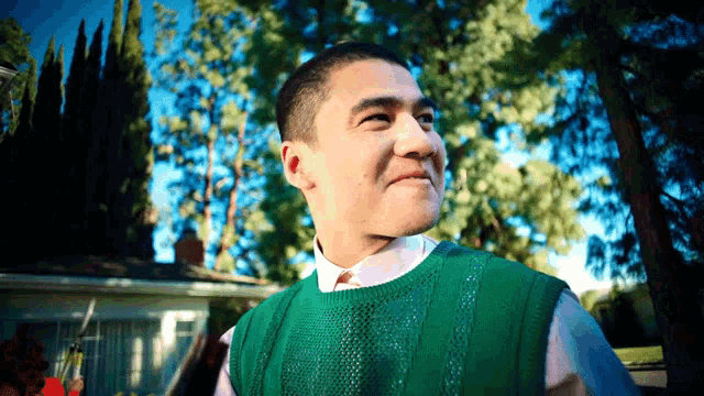 a man wearing a green vest and a white shirt is standing in front of a house