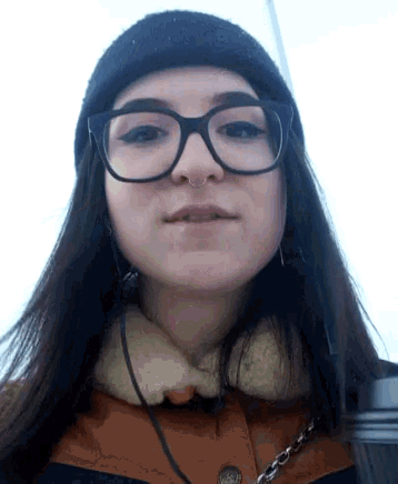 a woman wearing glasses and a beanie is looking at the camera