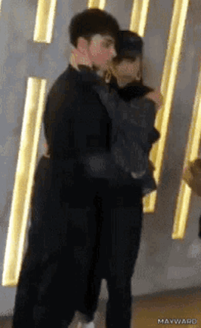 a man is holding a woman in his arms in front of a wall with gold stripes