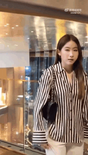 a woman wearing a black and white striped shirt and white pants is standing in front of a building .