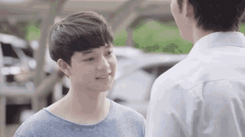 two young men are standing next to each other in a parking lot and looking at each other .