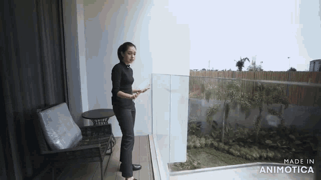 a woman is standing on a balcony with a glass railing and looking out the window .