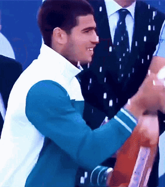 a man in a blue and white jacket is smiling while holding a trophy