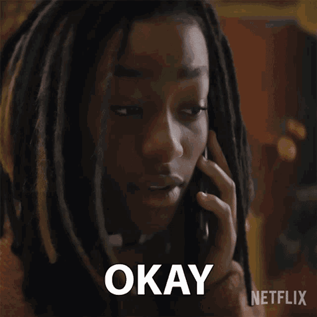 a woman with dreadlocks is talking on a cell phone and the word okay is on the screen