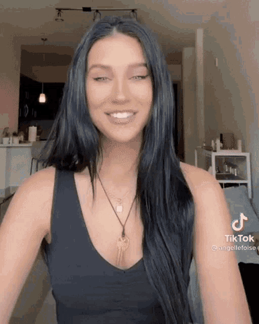 a woman with long black hair is wearing a black tank top and a necklace with two keys on it .