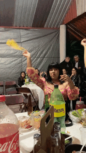 a bottle of fresca sits on a table next to a woman holding a fan