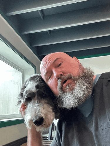 a bald man with a beard is holding a small dog on his shoulder