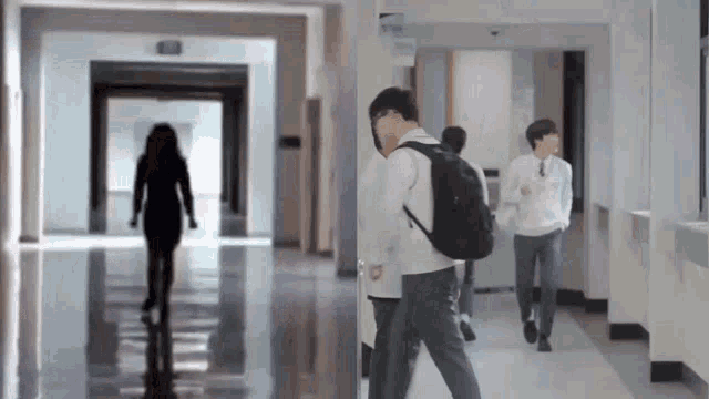 a group of people are walking down a hallway and one of them has a backpack .