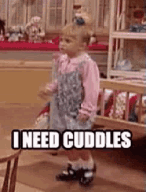 a little girl is standing in a room with a crib and a sign that says `` i need cuddles '' .