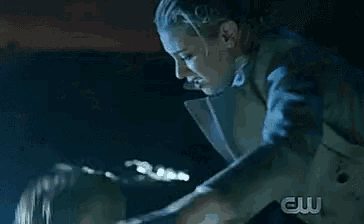 a woman is holding another woman in a dark room with a cw logo on the bottom right