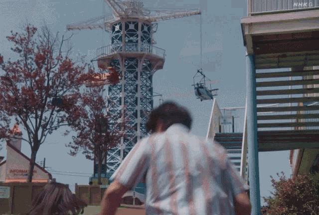 a man in a striped shirt is walking in front of a nhk building
