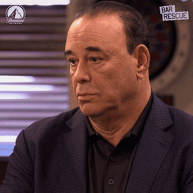 a man in a suit and black shirt is sitting in front of a paramount logo