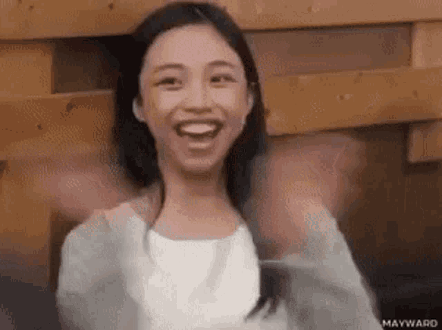 a young woman is smiling and waving her arms in front of a wooden wall .
