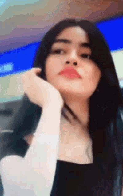 a woman with long black hair is looking at the camera with her hand on her face .