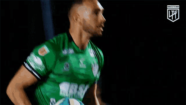 a man in a green jersey is holding a soccer ball in his hands .