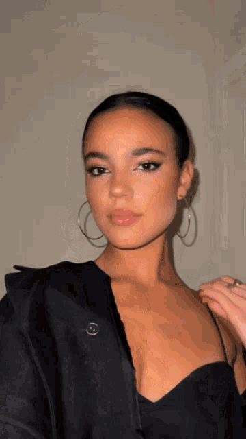 a woman wearing a black dress and hoop earrings looks at the camera