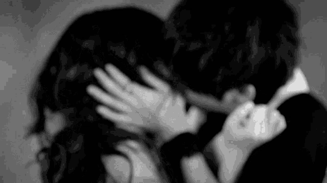 a black and white photo of a man and a woman kissing .