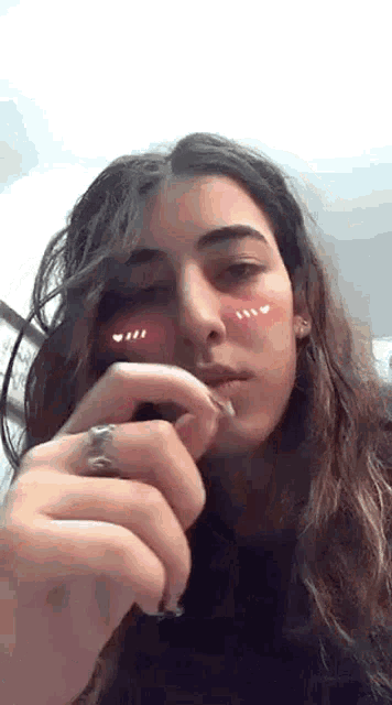 a close up of a woman 's face with a ring on her finger and hearts on her cheeks .